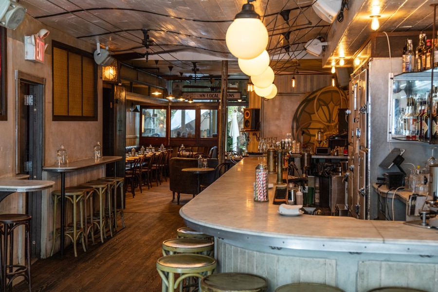 The long zinc-topped bar, globe lamps and round stained-glass window at St. Mazie in Williamsburg