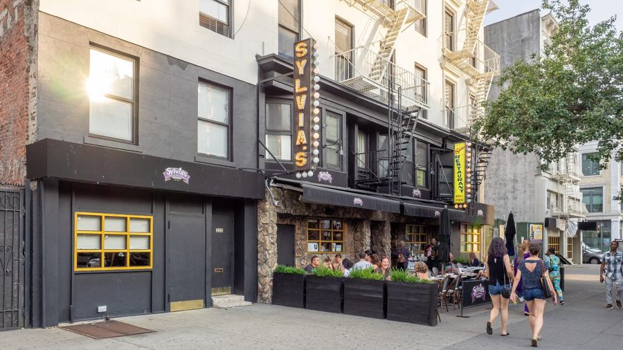 Sylvia's Restaurant in Harlem, with its tall marquee-bulb vertical signs, stone facade and sidewalk dining planters on Malcolm X Boulevard.