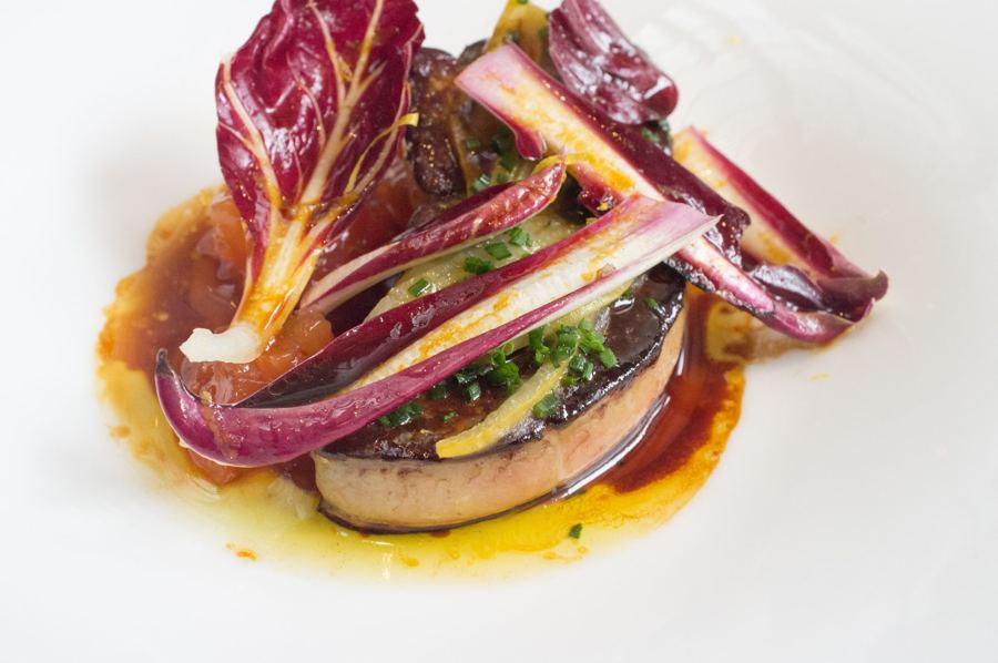 A plated slice of roasted foie gras topped with ribbons of red endive in a glossy citrus sauce on a white plate at The Modern.