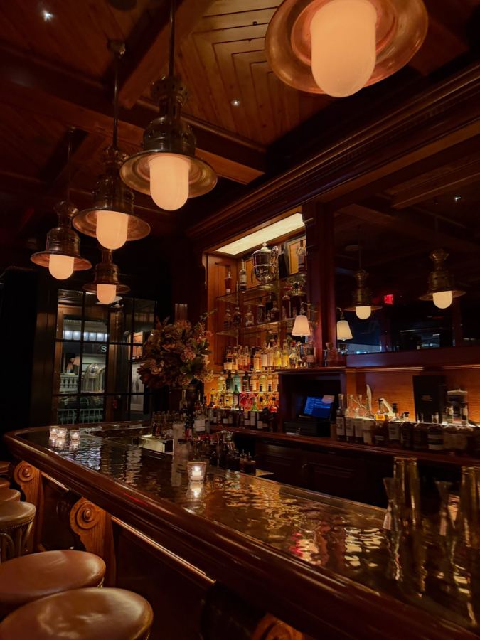 The Polo Bar's curved wooden bar under brass ship's lamps, candles glowing on the hammered-copper bar top and bottles lit along the back bar