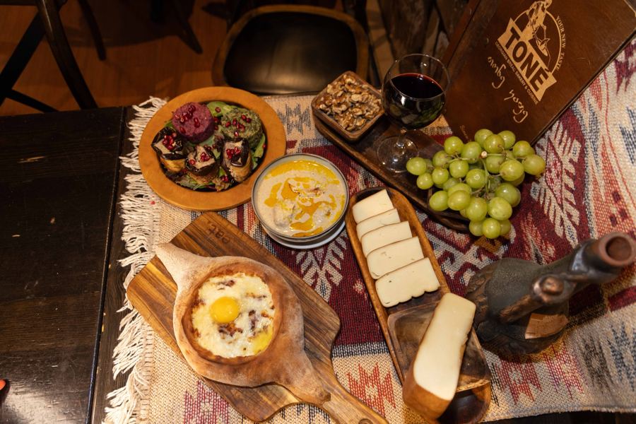 A boat-shaped adjaruli khachapuri with a bright egg yolk beside a long loaf of puri from the clay tone oven at Toné Café