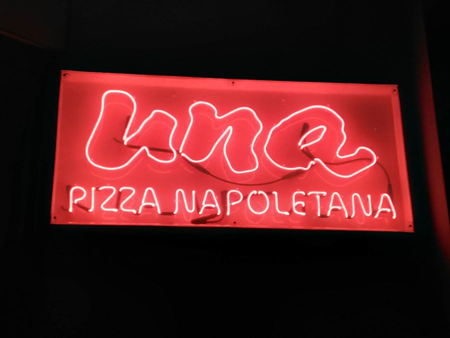 The red neon "una Pizza Napoletana" sign glowing in the window of the Orchard Street pizzeria