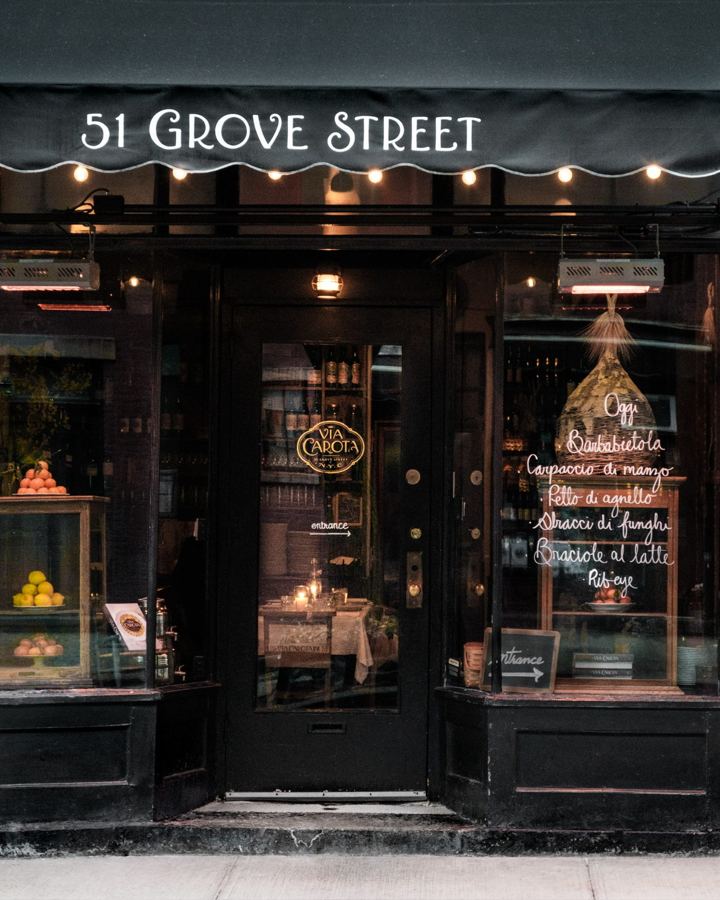 The dark wood facade of Via Carota at 51 Grove Street, with a scalloped awning, a glowing doorway and a chalk-written menu in the window.