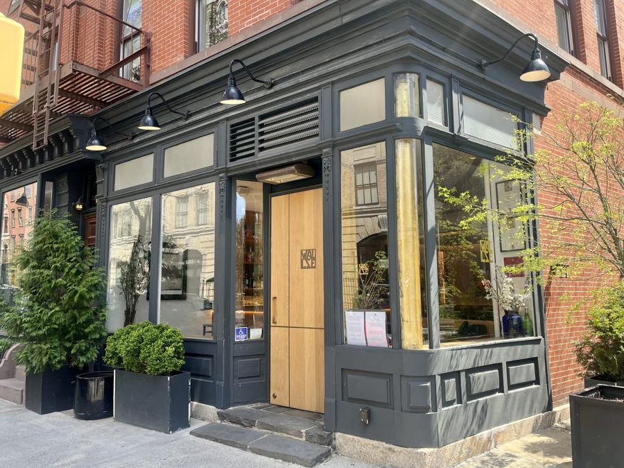 The dark-painted corner storefront of Wallsé in the West Village, with a pale wooden door, gooseneck lamps and potted boxwoods.