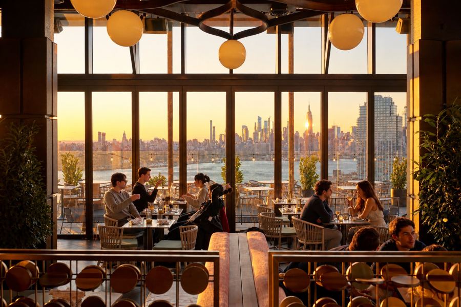 Diners at golden hour inside Westlight, with floor-to-ceiling windows framing the Manhattan skyline