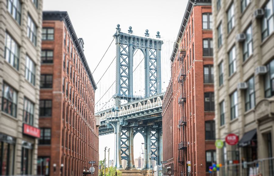 Manhattan Bridge tower centered over cobblestoned Washington Street between brick warehouses in DUMBO