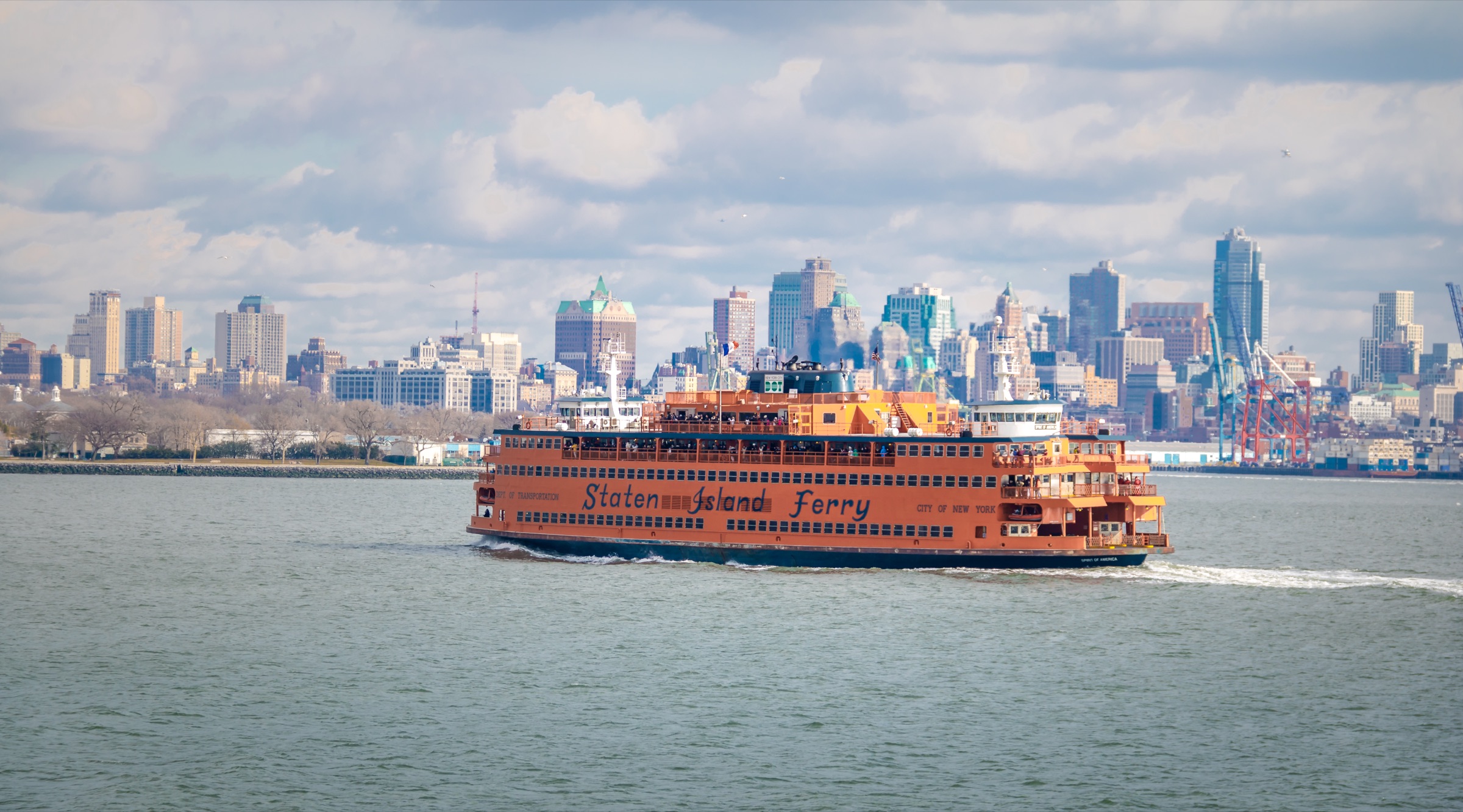 The orange Staten Island Ferry crossing New York Harbor with the lower Manhattan skyline behind it