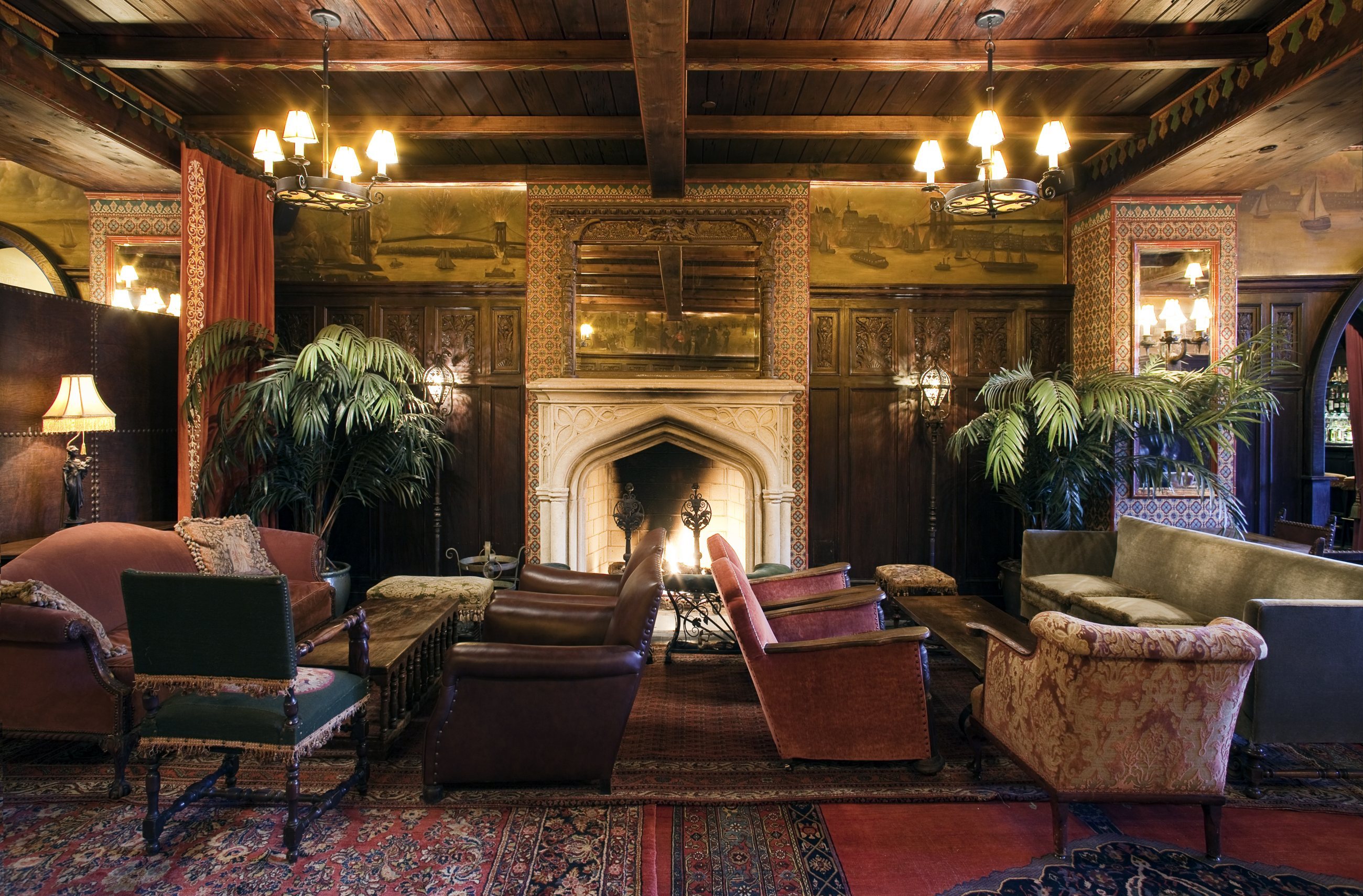 The fireplace lobby at The Bowery Hotel: wood-beamed ceiling, velvet armchairs, palms and Persian rugs