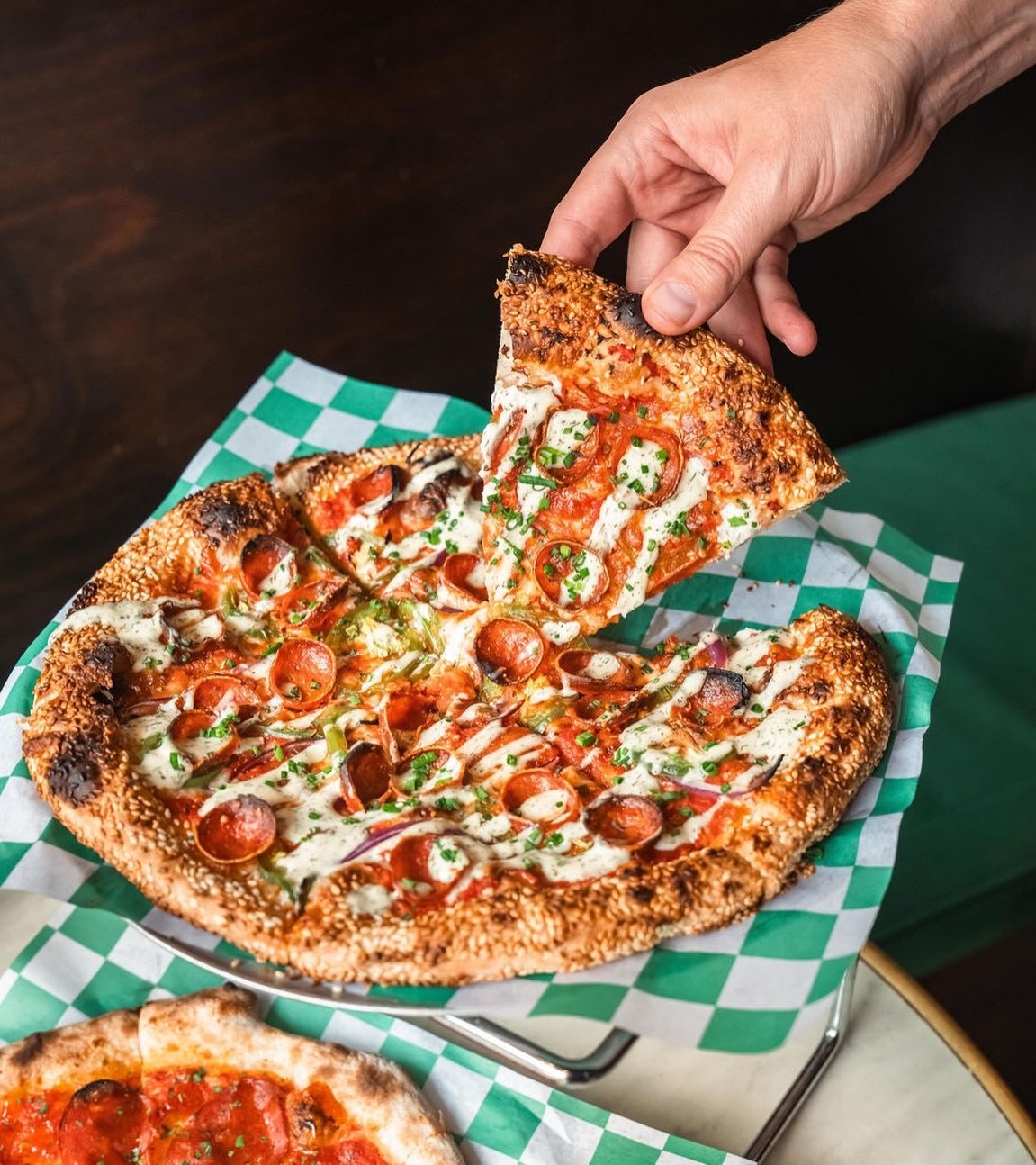 A thin pepperoni pizza with white sauce and a sesame crust lifted from the tray at Bar Birba