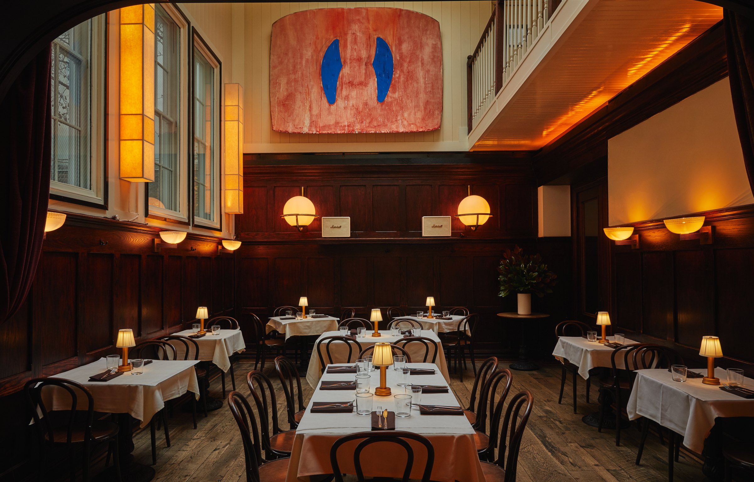 F&F Restaurant & Bar's wood-paneled dining room, white tablecloths lit by small lamps under a large painting