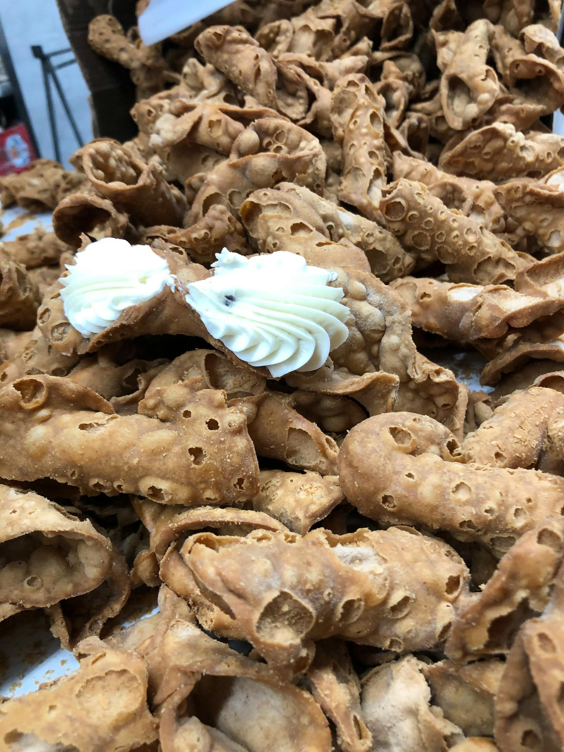 A pile of fried cannoli shells, two filled with cream, at Fortunato Brothers