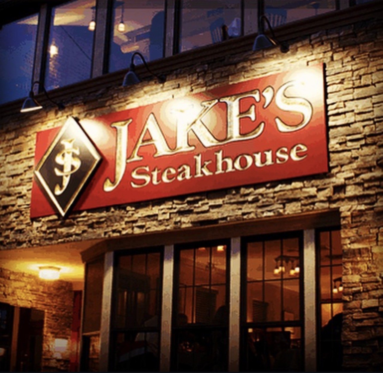 Jake's Steakhouse sign glowing on its stacked-stone front on Broadway, the windows lit above