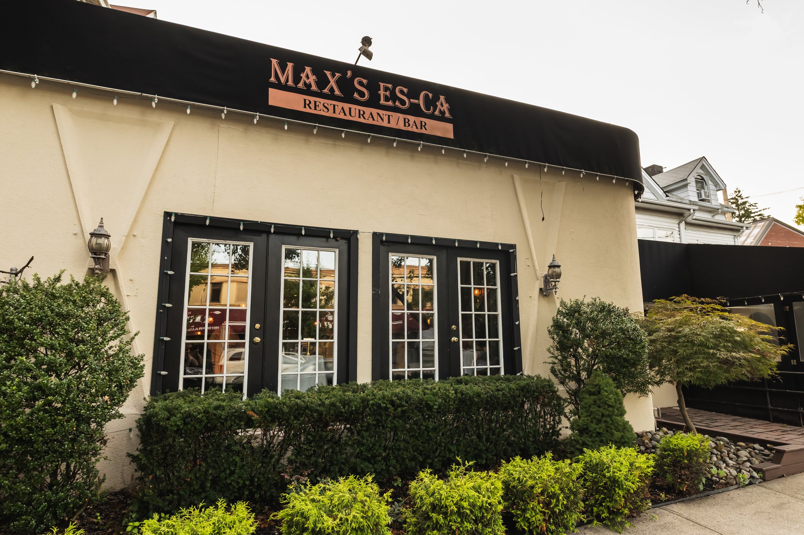 The cream-colored front of Max's Es-Ca on Richmond Road, with its awning sign and hedges