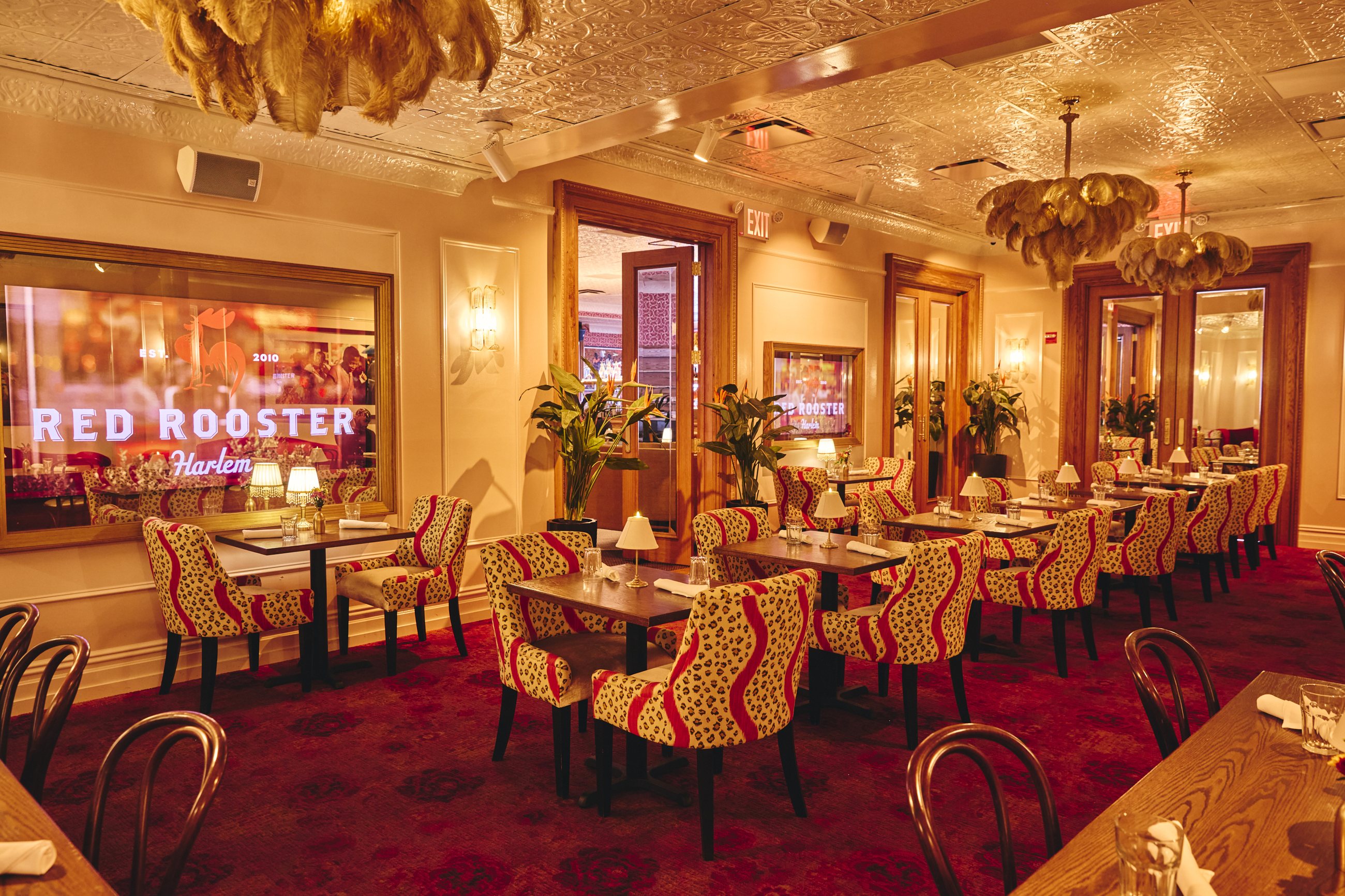 The Gold Room at Red Rooster Harlem — gilded chandeliers, red-patterned chairs and a glowing Red Rooster sign