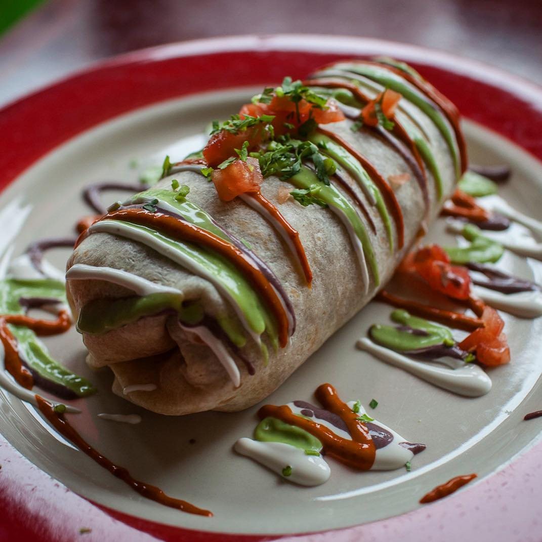 A burrito striped with green and red sauces on a plate at Taqueria Tlaxcalli