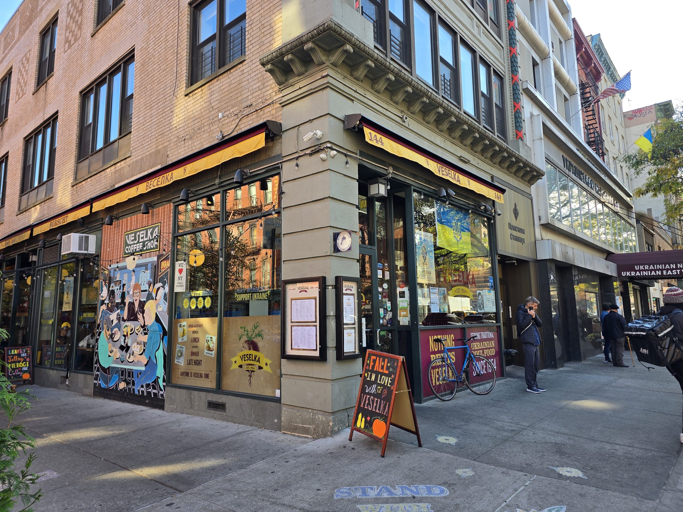 The corner storefront of Veselka in the East Village, with its yellow sign band, painted windows and a sidewalk chalkboard.