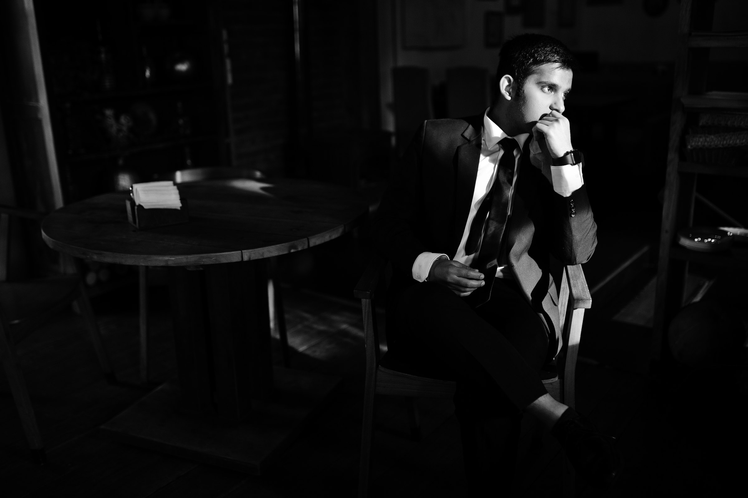 A man in a dark suit at a café table in a dim old-fashioned room, in black and white