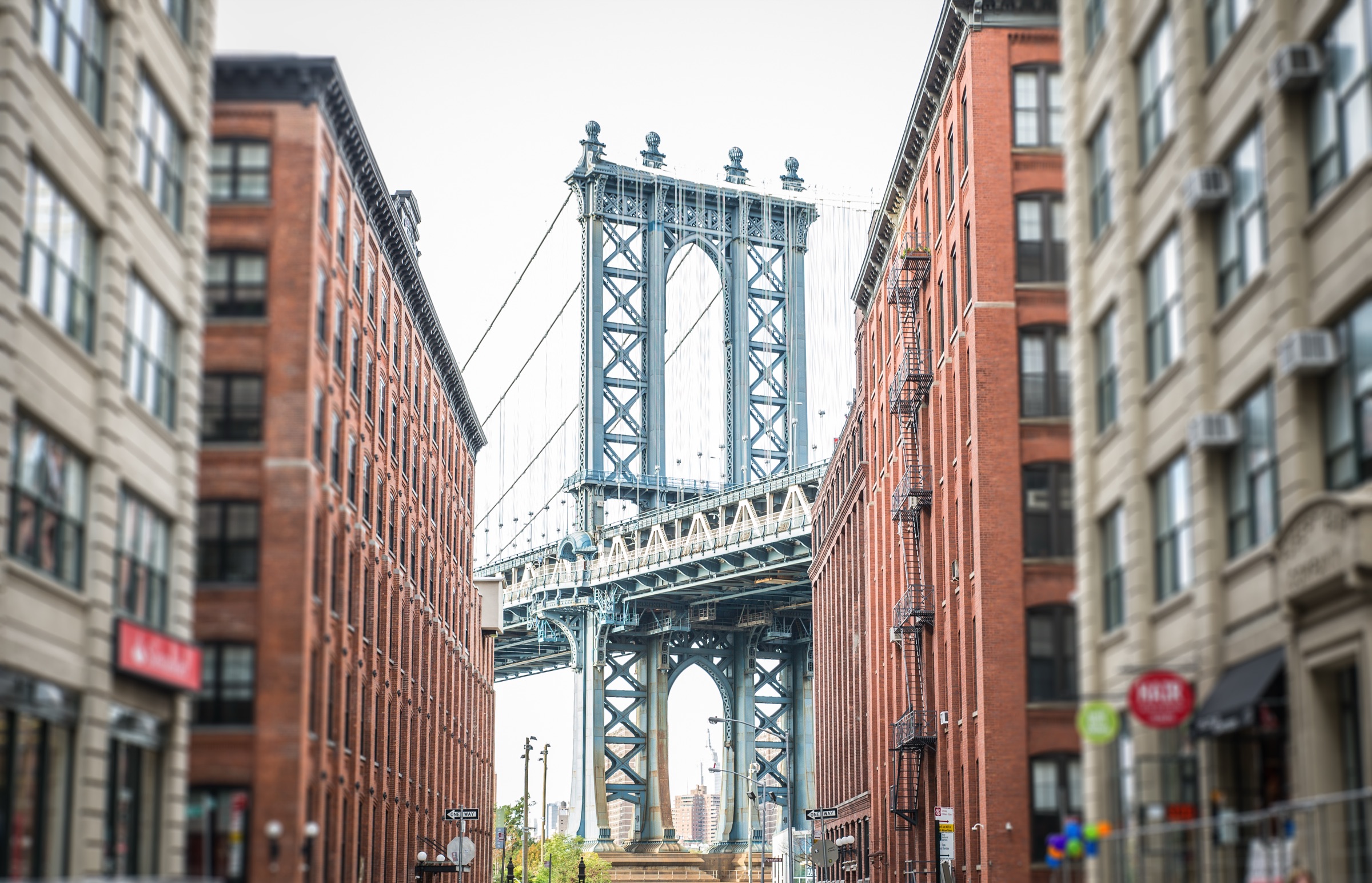 Manhattan Bridge tower centered over cobblestoned Washington Street between brick warehouses in DUMBO