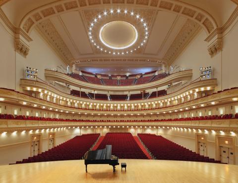 Stern Auditorium at Carnegie Hall seen from the stage, a grand piano in front of the red seats and five gilded tiers rising to the oval ceiling