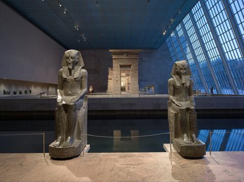 The Temple of Dendur in its glass-walled gallery at the Metropolitan Museum of Art, flanked by two seated statues